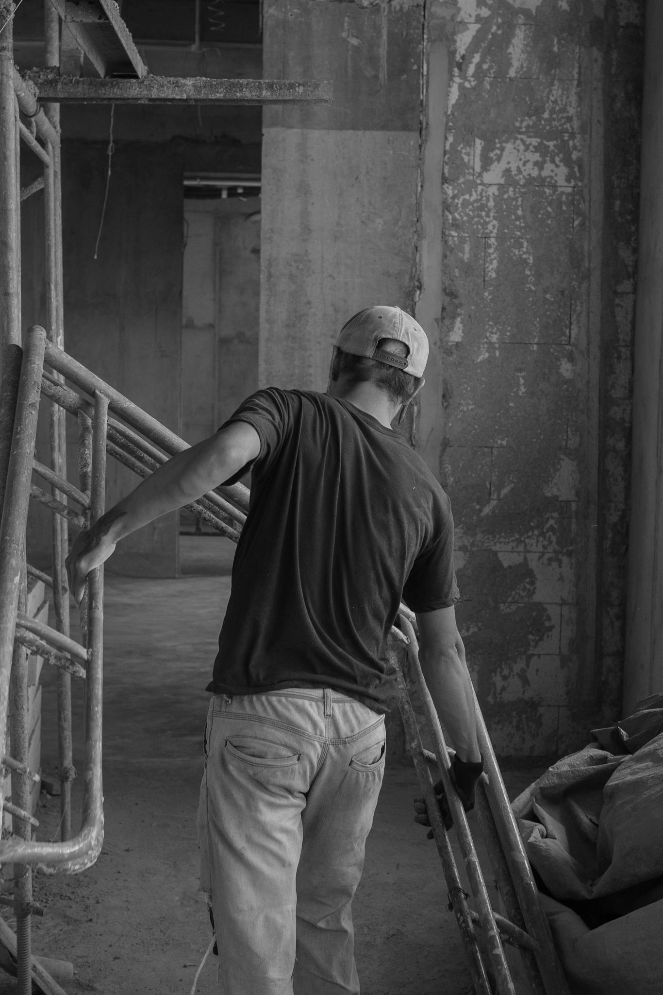 Worker adjusting scaffolding in an industrial indoor setting captured in monochrome.